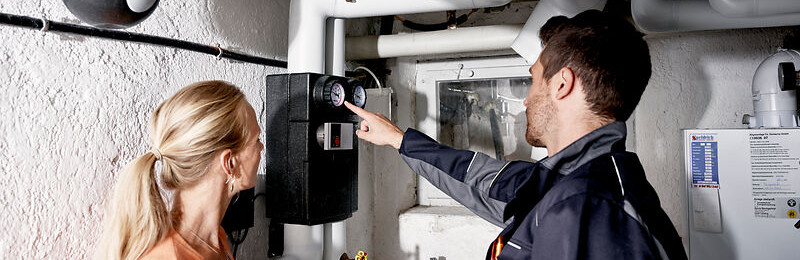 Eine Frau und ein Mann stehen im Keller vor einem Zähler.