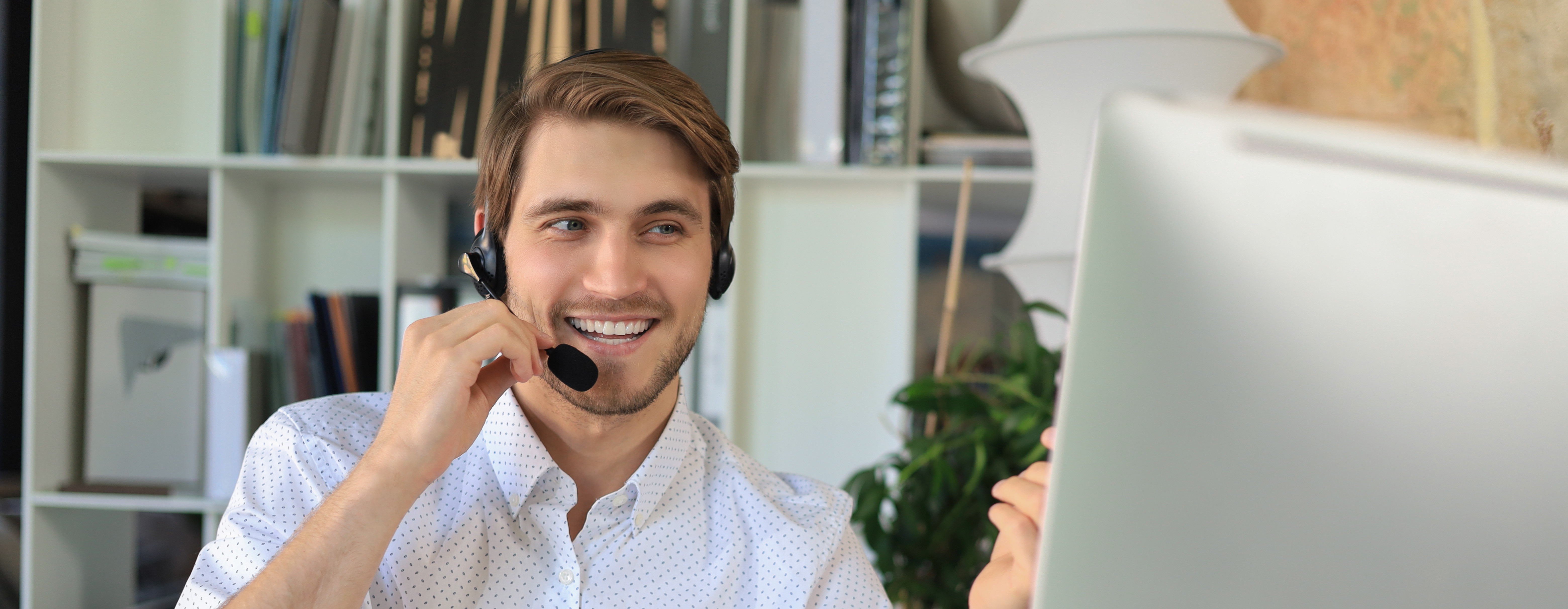 Ein Mann mit Headset schaut auf einen Bildschirm, im Hintergrund ist ein Regal mit Heftern